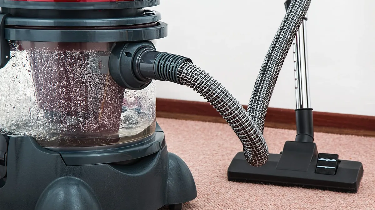 Close-up of professional cleaning equipment with a hose and cleaning head resting on the carpet pile